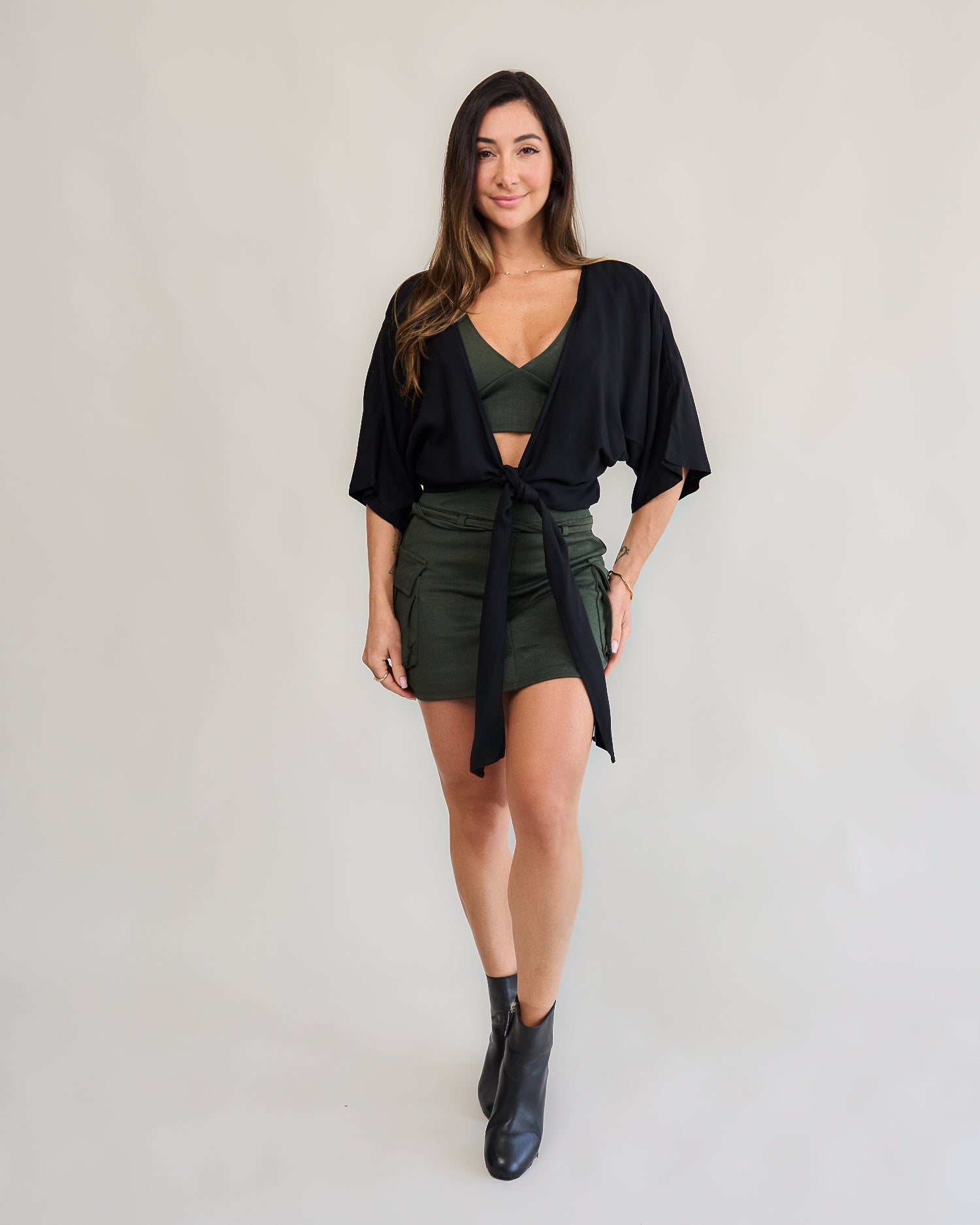 Short saia cargo verde militar feminino look com camisa amarração preta contraste bota preta